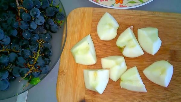 Грозди синего винограда и кусочки яблок на деревянной разделочной доске