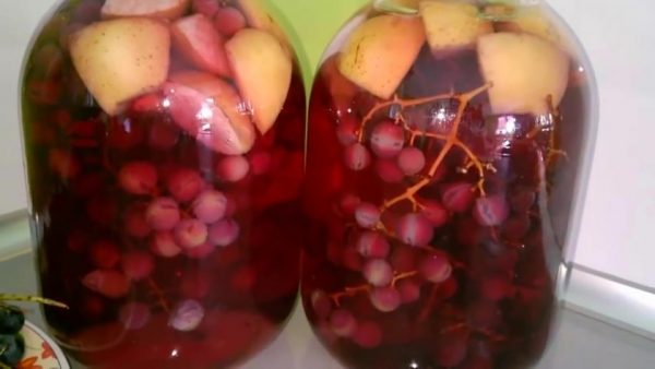 Большие стеклянные банки с компотом из винограда и яблок на столе